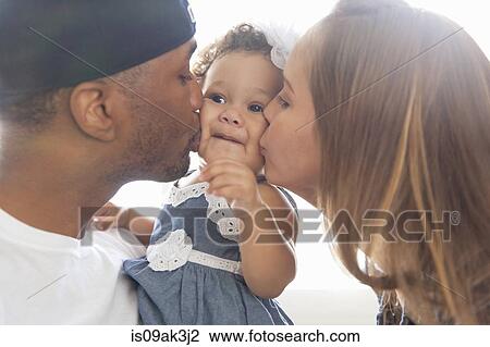 Stock Image - Mother and father kissing young daughter on cheeks. Fotosearch