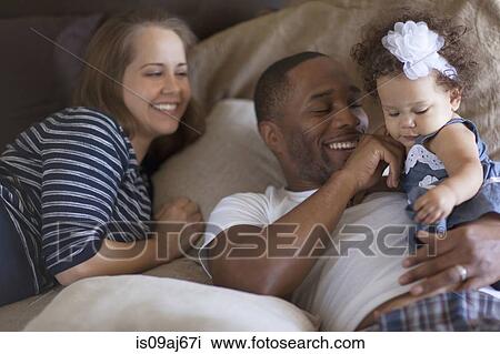 Mother and father lying on bed with baby daughter View Large Photo Image Stock Image - Mother and father lying on bed with baby daughter. Fotosearch