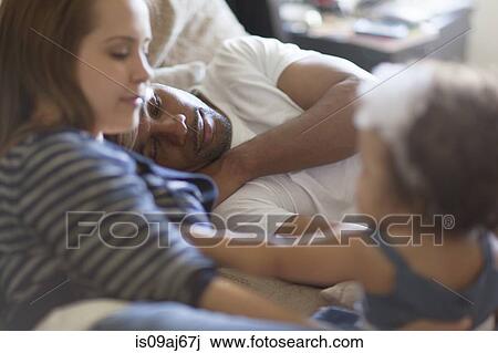 Stock Image - Mother and father lying on bed with baby daughter. Fotosearch