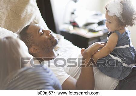 Stock Photography - Mother and father lying on bed with baby daughter. Fotosearch