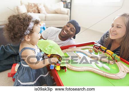 Stock Photography - Mother and father playing with young daughter, train set on table. Fotosearch