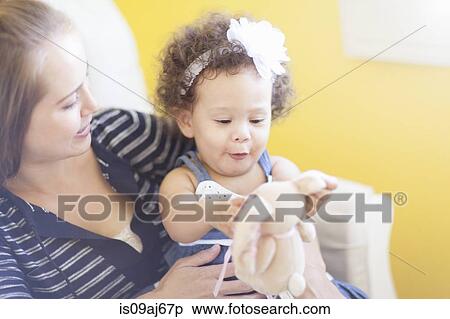 Stock Photography - Mother holding baby daughter, playing with soft toy. Fotosearch