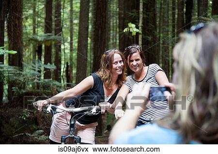 Over shoulder view of women mountain bikers posing for photograph on smartphone in forest View Large Photo Image Stock Photo - Over shoulder view of women mountain bikers posing for photograph on smartphone in forest. Fotosearch