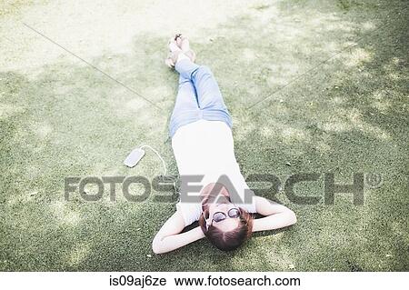Overhead view of mid adult woman lying down and listening to earphones in park View Large Photo Image Stock Image - Overhead view of mid adult woman lying down and listening to earphones in park. Fotosearch