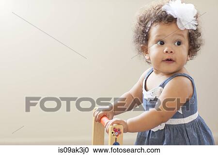 Stock Image - Portrait of baby girl, pushing baby walker. Fotosearch