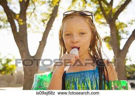 Stock Photo - Portrait of girl eating ice lolly in garden. Fotosearch