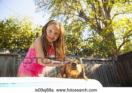 Stock Image - Portrait of girl petting dog in garden paddling pool. Fotosearch