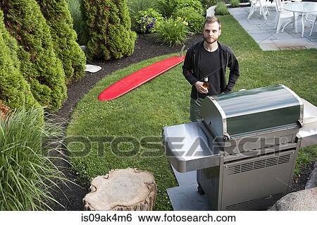 Portrait of mid adult man standing by barbecue with bottle of beer in garden View Large Photo Image Stock Photograph - Portrait of mid adult man standing by barbecue with bottle of beer in garden. Fotosearch