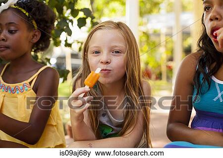 Portrait of three girls eating ice lollies in garden View Large Photo Image Stock Photo - Portrait of three girls eating ice lollies in garden. Fotosearch