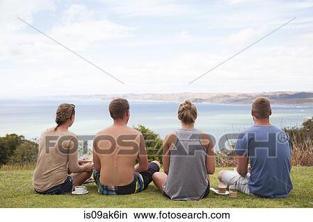 Rear view of four friends sitting looking away to sea View Large Photo Image Picture - Rear view of four friends sitting looking away to sea. Fotosearch
