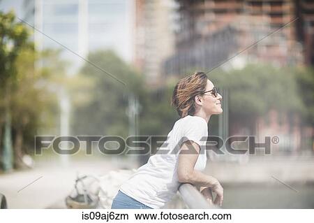Picture - Smiling mid adult woman leaning on city railings. Fotosearch