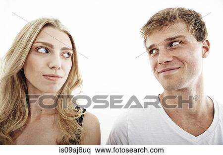 Stock Photography - Studio portrait of young couple looking sideways at each other. Fotosearch