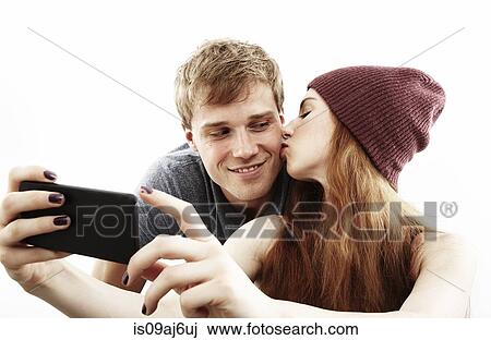 Stock Image - Studio portrait of young couple taking selfie on smartphone. Fotosearch