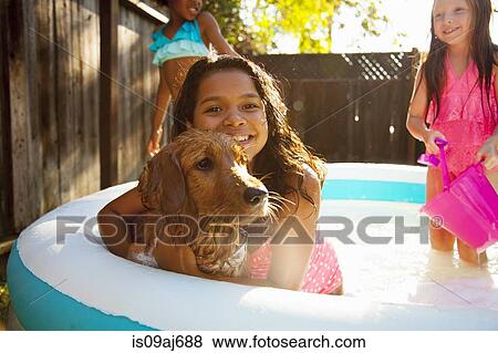 Stock Photo - Three girls and a dog in garden paddling pool. Fotosearch