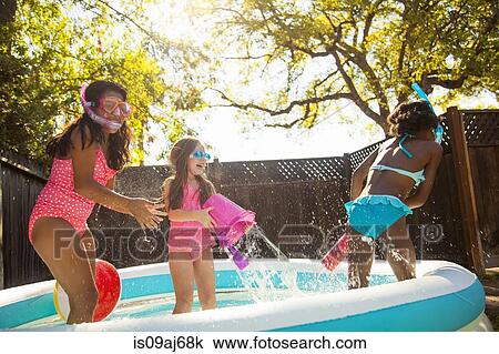 Stock Image - Three girls playing and splashing in garden paddling pool. Fotosearch