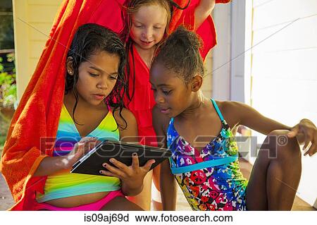 Stock Image - Three girls wrapped in towel on porch looking at digital tablet. Fotosearch