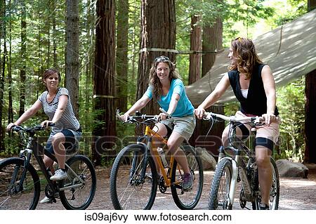 Stock Photo - Three women mountain bikers cycling in forest. Fotosearch