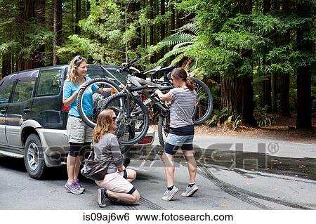 Stock Photograph - Three women mountain bikers lifting bikes from four wheel vehicle in forest. Fotosearch