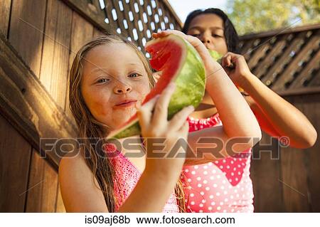 Stock Image - Two girls eating slices of watermelon in garden. Fotosearch
