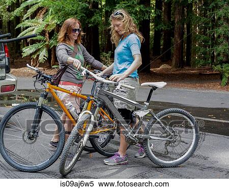 Two women mountain bikers preparing to cycle in forest View Large Photo Image Stock Photography - Two women mountain bikers preparing to cycle in forest. Fotosearch
