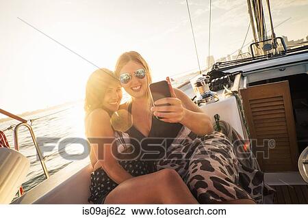 Stock Photo - Two women on yacht using smartphone. Fotosearch
