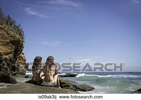 Two young women sitting on rocks, looking out to ocean View Large Photo Image Stock Image - Two young women sitting on rocks, looking out to ocean. Fotosearch