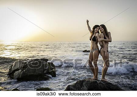 Two young women standing on rock in ocean View Large Photo Image Stock Image - Two young women standing on rock in ocean. Fotosearch