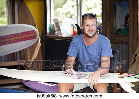 Young male surfer sitting in shed waxing his surfboard View Large Photo Image Stock Photo - Young male surfer sitting in shed waxing his surfboard. Fotosearch