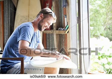 Young male surfer sitting in shed waxing surfboard View Large Photo Image Stock Photo - Young male surfer sitting in shed waxing surfboard. Fotosearch