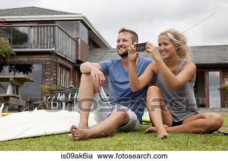 Stock Image - Young surfer couple photographing with smartphone. Fotosearch
