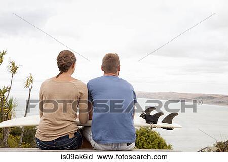 Young surfing couple sitting on picnic bench looking away to sea View Large Photo Image Stock Image - Young surfing couple sitting on picnic bench looking away to sea. Fotosearch