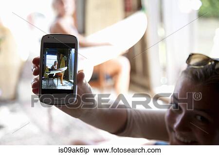 Stock Photography - Young woman holding up smartphone with photograph of her best friend. Fotosearch