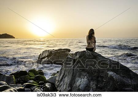 Young woman sitting on rock in ocean, rear view View Large Photo Image Stock Image - Young woman sitting on rock in ocean, rear view. Fotosearch