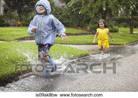 Boy and sister wearing rubber boots running and splashing in rain puddle View Large Photo Image Stock Photo - Boy and sister wearing rubber boots running and splashing in rain puddle. Fotosearch