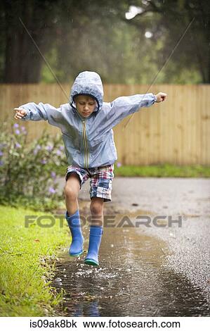 Stock Image - Boy in rubber boots jumping in rain puddle. Fotosearch