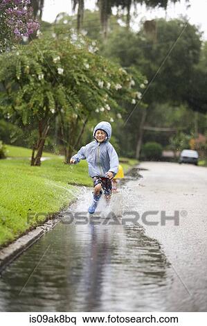 Stock Photography - Boy in rubber boots running and splashing in rain puddle. Fotosearch
