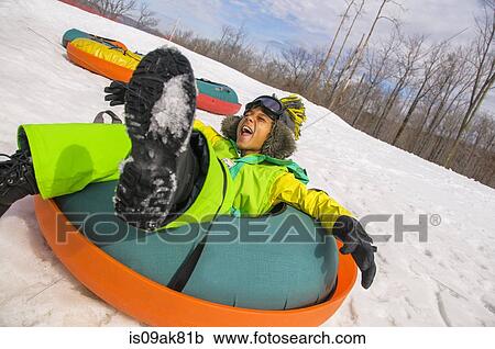 Stock Image - Boy laughing whilst tobogganing down snowy hill. Fotosearch