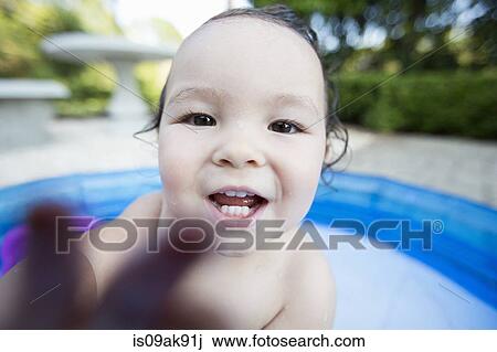 Stock Image - Close up candid portrait of a baby girl in paddling pool. Fotosearch