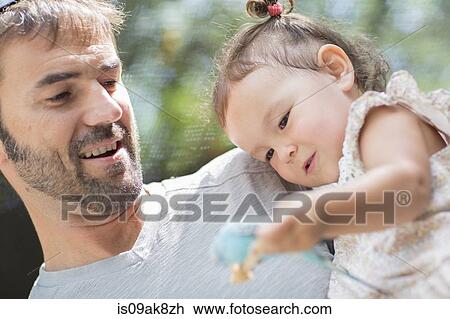 Stock Image - Close up of father and baby daughter holding budgerigar parakeet at zoo. Fotosearch