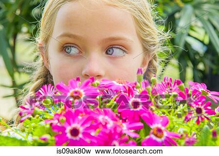 Stock Photo - Close up portrait of girl looking sideways behind pink flowers. Fotosearch