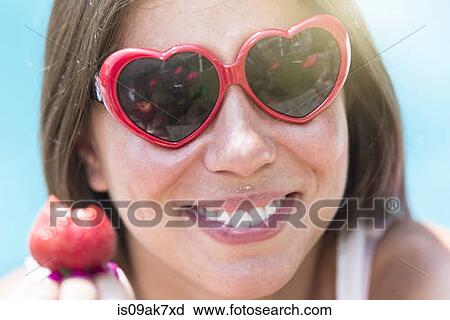 Stock Image - Close up portrait of young woman eating strawberry. Fotosearch