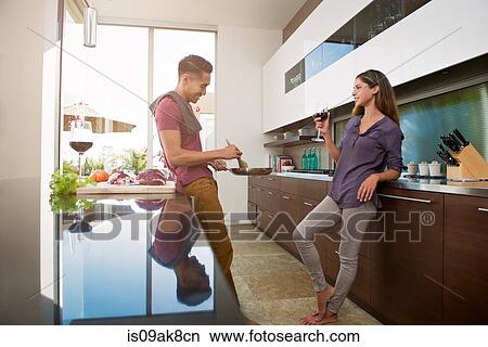 Couple chatting and drinking wine whilst cooking in kitchen View Large Photo Image Picture - Couple chatting and drinking wine whilst cooking in kitchen. Fotosearch