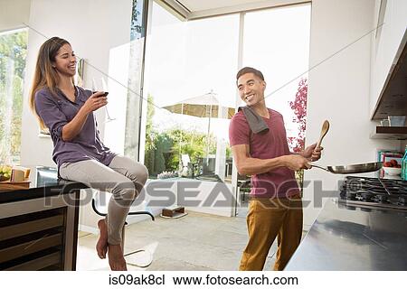 Stock Image - Couple laughing and fooling around whilst cooking in kitchen. Fotosearch