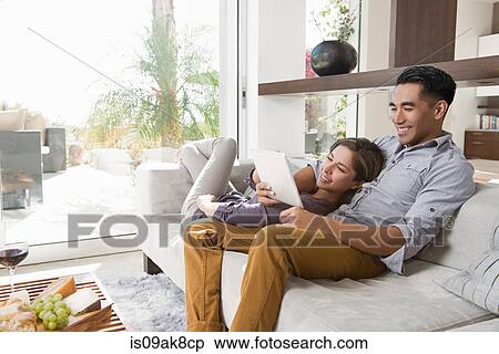 Couple on sitting room sofa looking at digital tablet View Large Photo Image Stock Photography - Couple on sitting room sofa looking at digital tablet. Fotosearch