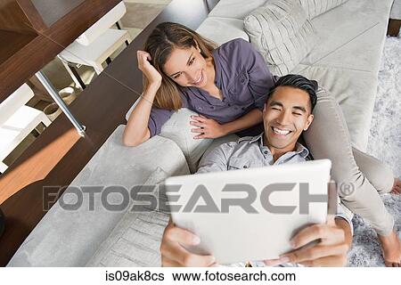 Couple on sitting room sofa taking selfie with digital tablet View Large Photo Image Stock Photograph - Couple on sitting room sofa taking selfie with digital tablet. Fotosearch