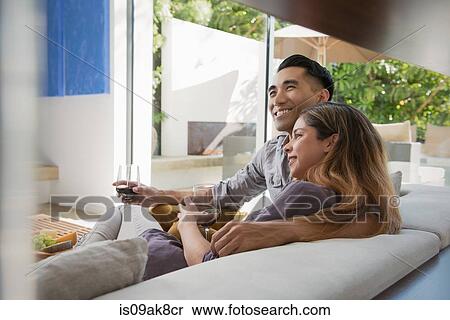 Stock Photography - Couple relaxing together with glass of red wine on sitting room sofa. Fotosearch