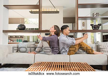 Couple sitting back to back playing games on smartphones on sitting room sofa View Large Photo Image Stock Photo - Couple sitting back to back playing games on smartphones on sitting room sofa. Fotosearch