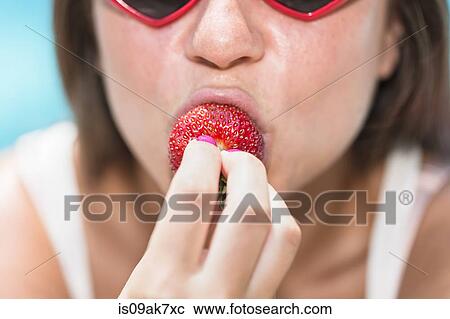 Stock Image - Cropped portrait of young woman biting strawberry. Fotosearch