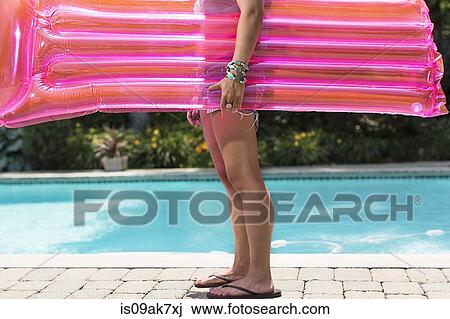 Stock Image - Cropped shot of young woman carrying airbed at poolside. Fotosearch