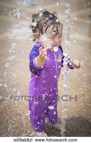 Stock Image - Cute baby girl with eyes closed getting sprinkled with water. Fotosearch